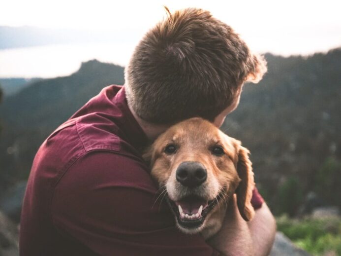 photo of man hugging tan dog