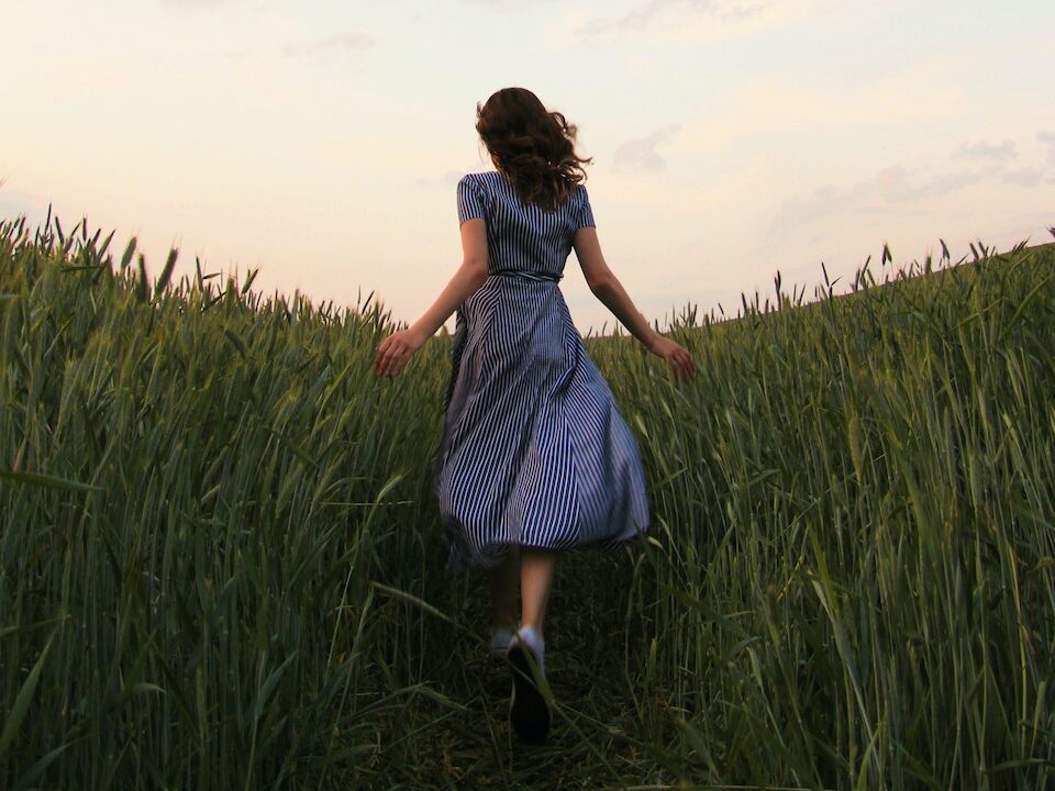Woman in Blue Striped Dress Running on the Green Grass Field