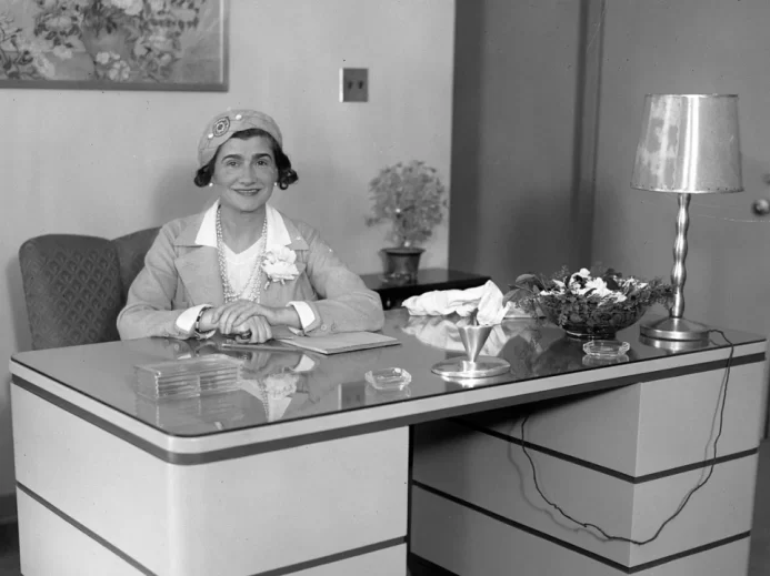 Coco Chanel sedící za stolem