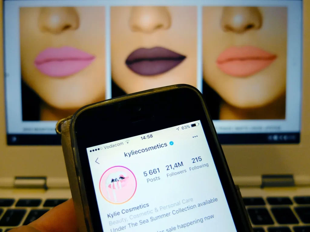 Náhled na mobilu na Instagram Kylie a v pozadí náhled prodávaných odstínů rtěnek