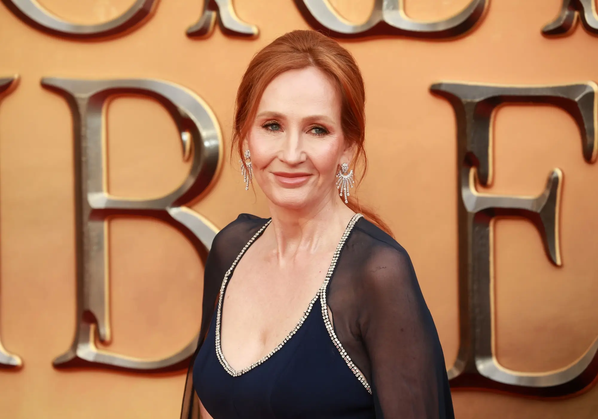 J. K. Rowling v černých večerních šatech na žlutém pozadí.