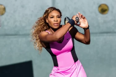 Serena na kjurtu v růžových šatech a raketou při odpalu