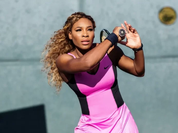 Serena na kjurtu v růžových šatech a raketou při odpalu