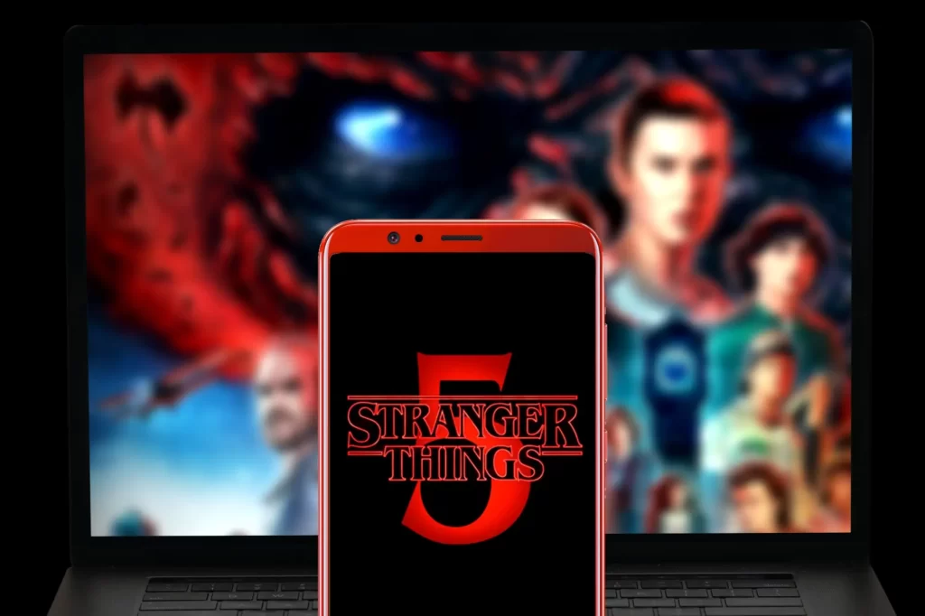 Mobilní telefon s červenou pětkou na displeji, v pozadí plakát na Stranger Things