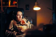 Žena v setmělé místnosti sleduje film a jí popcorn