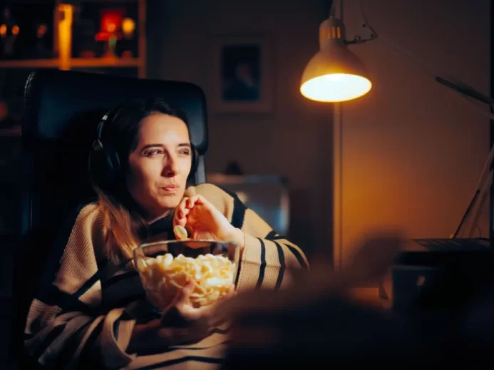 Žena v setmělé místnosti sleduje film a jí popcorn