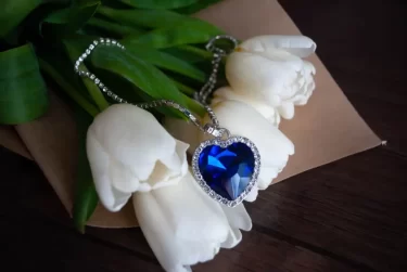 Modrý srdcový náhrdelník posázený diamanty položený na bílých tulipánech