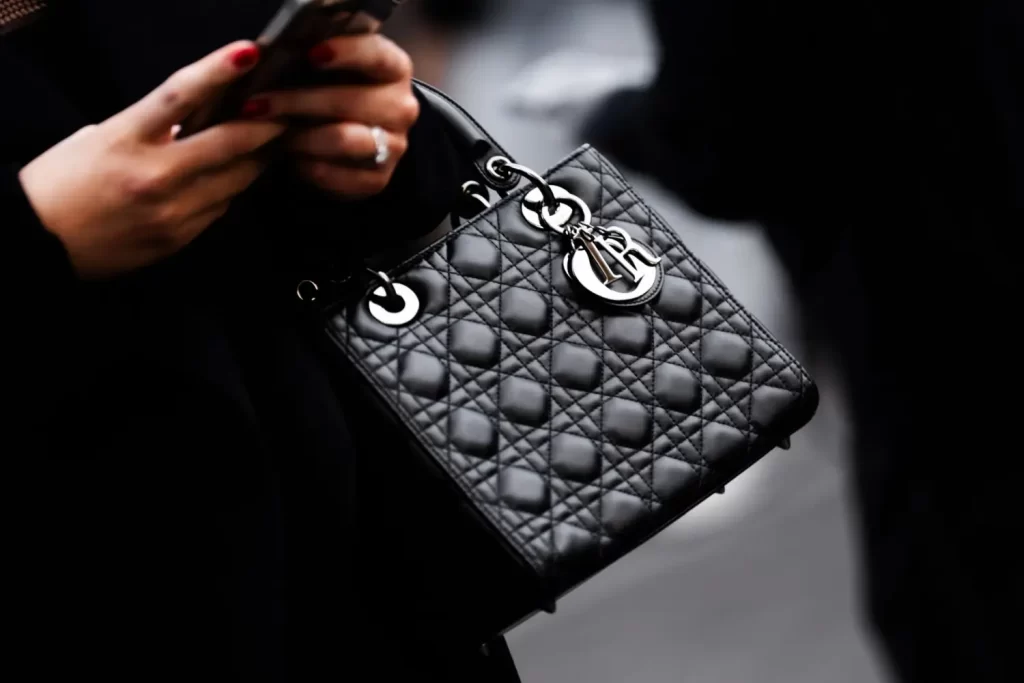 - VIPshow Kabelka Lady Dior v černé barvě se stříbrnými přívěsky v ruce elegantní ženy