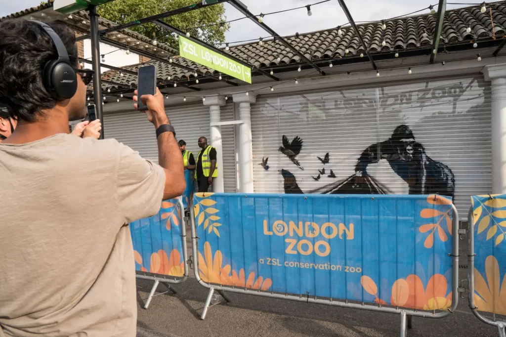 Návštěvníci Londýnské zoo si fotí nové pouliční dílo na zavřených roletách pavilonu.