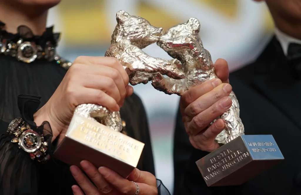 Dvě ruce držící stříbrné medvědy – sošky udělované na Berlinale.