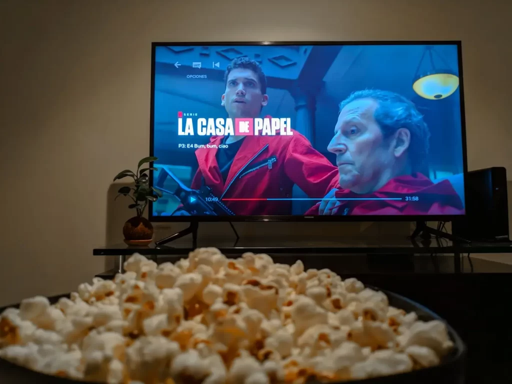 Scéna z populárního španělského seriálu La Casa de Papel na obrazovce televizoru s mísou popcornu v popředí