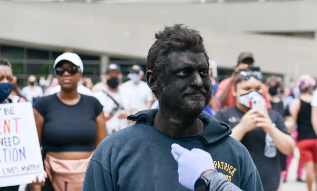 Bílý muž s načerněným obličejem během protestu 