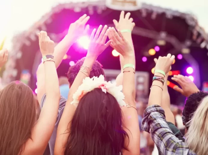 Hudba spojuje a tisíce lidí tančí jako jeden celek Skupina lidí se zvednutýma rukama tancuje před festivalovým pódiem osvětleným fialovými světly
