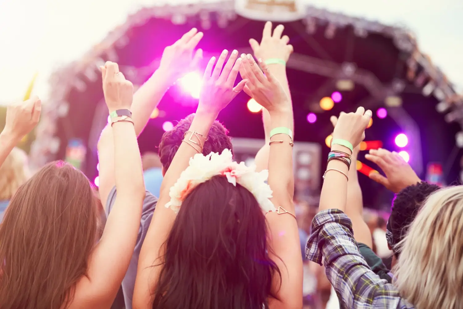 Skupina lidí se zvednutýma rukama tancuje před festivalovým pódiem osvětleným fialovými světly