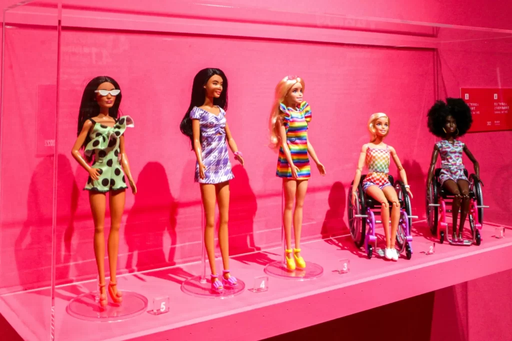 Kolekce moderních panenek Barbie vystavená ve skleněné vitríně s růžovým pozadím. 