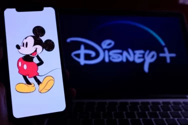 Ilustrace Mickeyho Mouse na mobilním telefonu před obrazovkou s logem Disney+