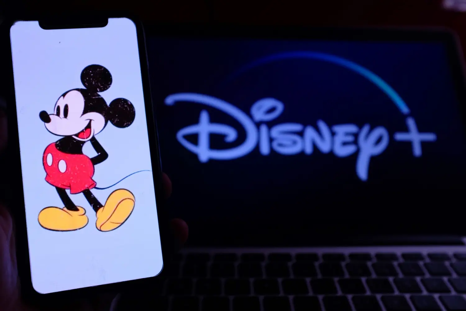 Ilustrace Mickeyho Mouse na mobilním telefonu před obrazovkou s logem Disney+