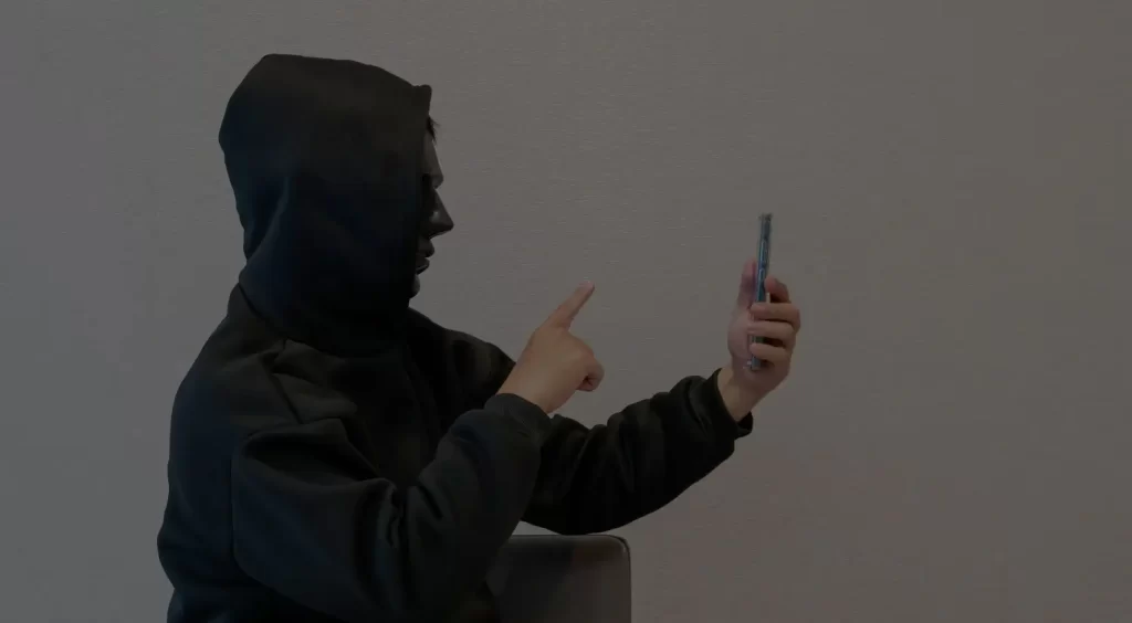 Osoba v černé mikině s kapucí sedí a natáčí se na chytrý telefon