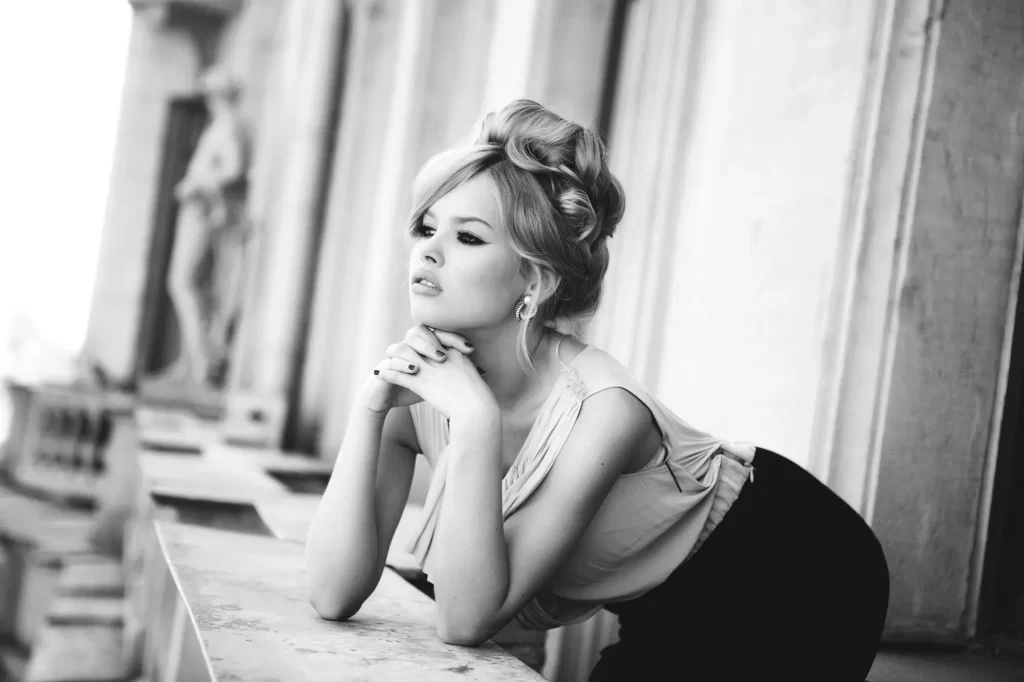 Retro portrét mladé ženy s účesem ve stylu Brigitte Bardot, naklánějící se přes zábradlí