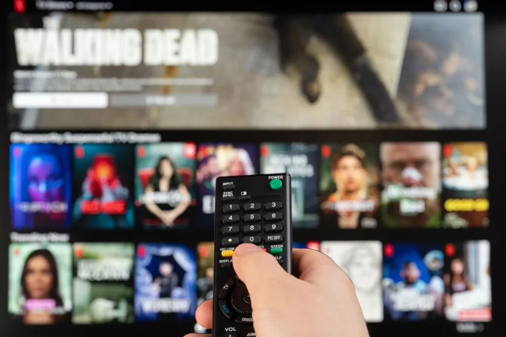 Ruka s ovladačem ukazuje na TV s výběrem filmů