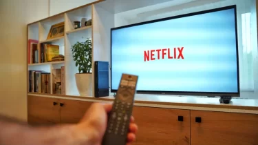 Mužská ruka s ovladačem ukazuje na obrazovku TV s logem Netflixu