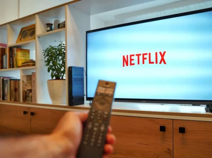 Mužská ruka s ovladačem ukazuje na obrazovku TV s logem Netflixu