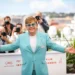 Elton John během fotografování na Filmovém festivalu v Cannes v roce 2019. Má na sobě tyrkysově modrý oblek s broží na klopě a bílé tričko. Jeho ikonické modré brýle s třpytivými obroučkami.
