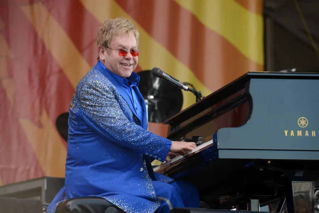 - VIPshow Elton John během živého vystoupení, sedí u černého koncertního klavíru.