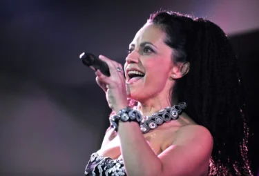 Lucie Bílá při energickém vystoupení s mikrofonem v ruce a výrazným šperkem na krku.