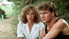 Man in a black sleeveless shirt and a white-blouse woman sit together on a park path, looking thoughtful.