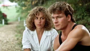 Man in a black sleeveless shirt and a white-blouse woman sit together on a park path, looking thoughtful.