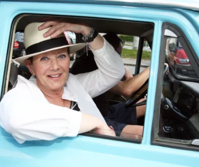 Žena si drží klobouk, sedí v automobilu