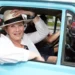 Žena si drží klobouk, sedí v automobilu