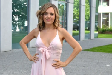 Mladá žena s dlouhými vlasy v romantických růžových šatech pózuje před fotografem