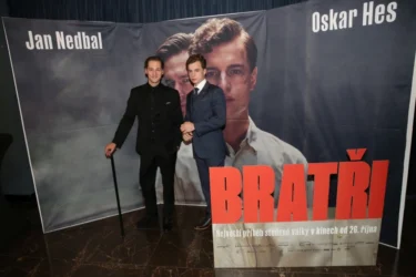 Dva muži v oblecích před plakátem s jejich portréty s nápisem Bratři