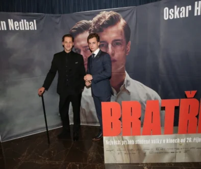 Dva muži v oblecích před plakátem s jejich portréty s nápisem Bratři