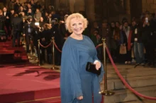 žena v modrých šatech se usmívá a pózuje na červeném koberci