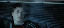 Person with round glasses and short dark hair lying down, looking off to the side against a blue striped background, nose ring visible.