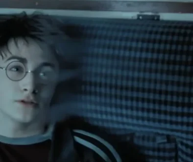 Person with round glasses and short dark hair lying down, looking off to the side against a blue striped background, nose ring visible.