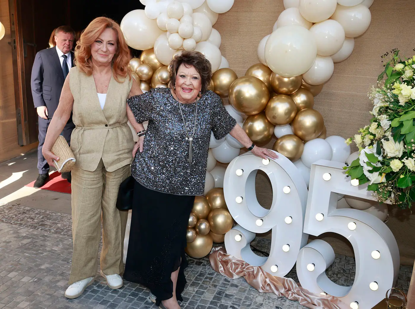 Dvě ženy stojí venku u velké číslovky 95 a kolem nich je spousta balonků