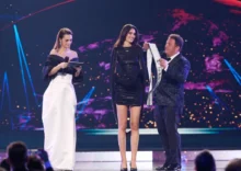 Tři lidé na pódiu, muž dává mladé dívce šerpu
