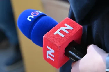 Ruka drží červeno-modrý mikrofon s bílými písmenky