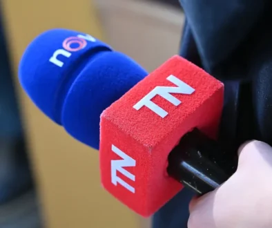 Ruka drží červeno-modrý mikrofon s bílými písmenky