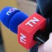 Ruka drží červeno-modrý mikrofon s bílými písmenky