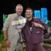 Two men smile on a stage, one holding a large 'SURVIVOR 2026' trophy between them.