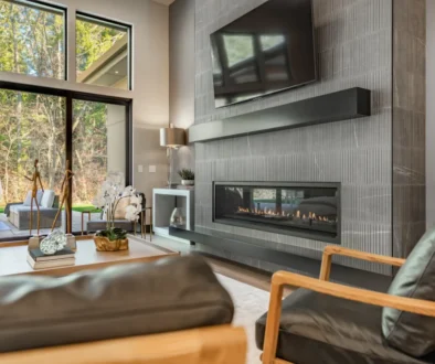 Modern living room with a built-in horizontal fireplace and textured gray tile wall, facing large glass doors to an outdoor seating area.