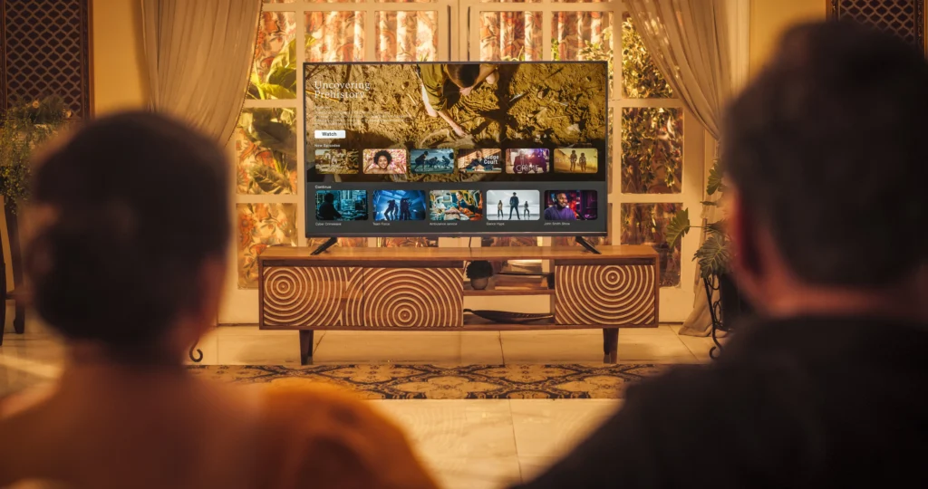 shutterstock_2312936887 - VIPshow Obývací pokoj. V něm se muž a žena, kteří sedí zády, dívají na velkou televizi