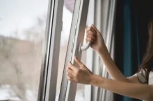 Close-up of a hand sliding a window latch to open a white transit window (bus/train) from inside the vehicle.