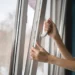 Close-up of a hand sliding a window latch to open a white transit window (bus/train) from inside the vehicle.
