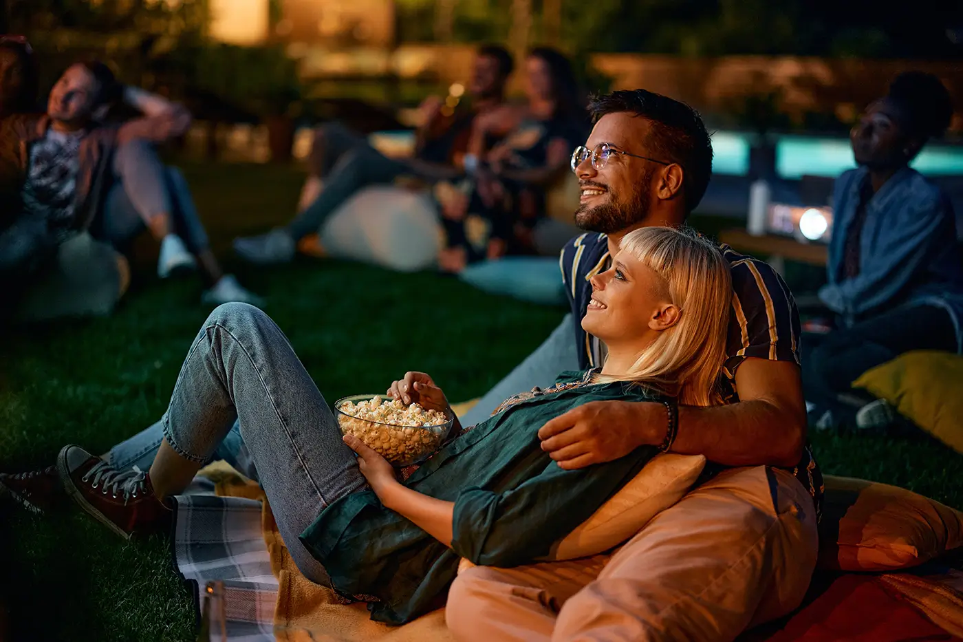 Mladý pár se po setmění dívá na film promítaný na plátně.